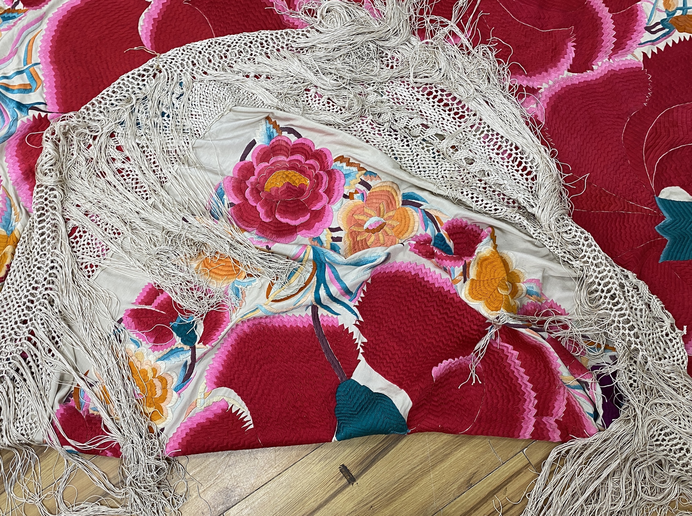 An unusual late 19th early 20th century Chinese cream silk shawl, embroidered with four huge bright pink and red flowers, surrounded with an embroidered floral border, all edged with a long cream silk tasselled fringe, 1